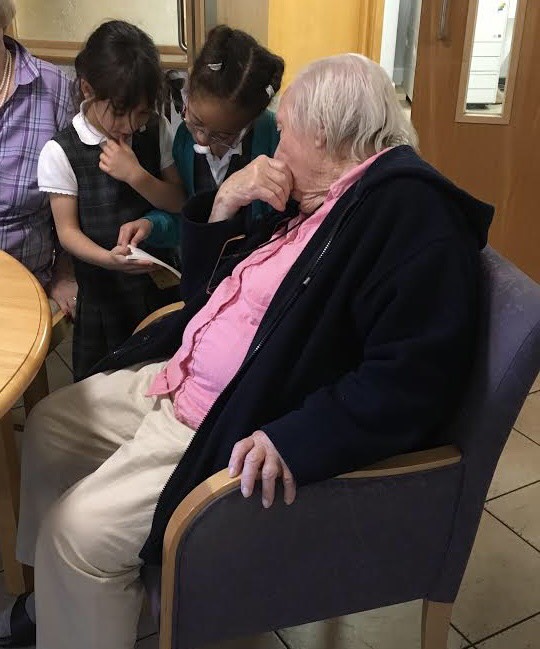 Two Year 2 pupils show a care home resident a book