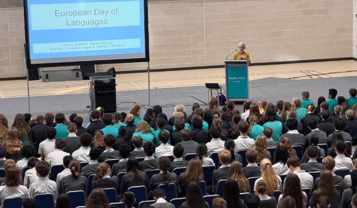 A woman stands behind a lectern speaking to a large audience of Stephen Perse Cambridge students about European Day or Languages 2026. 
